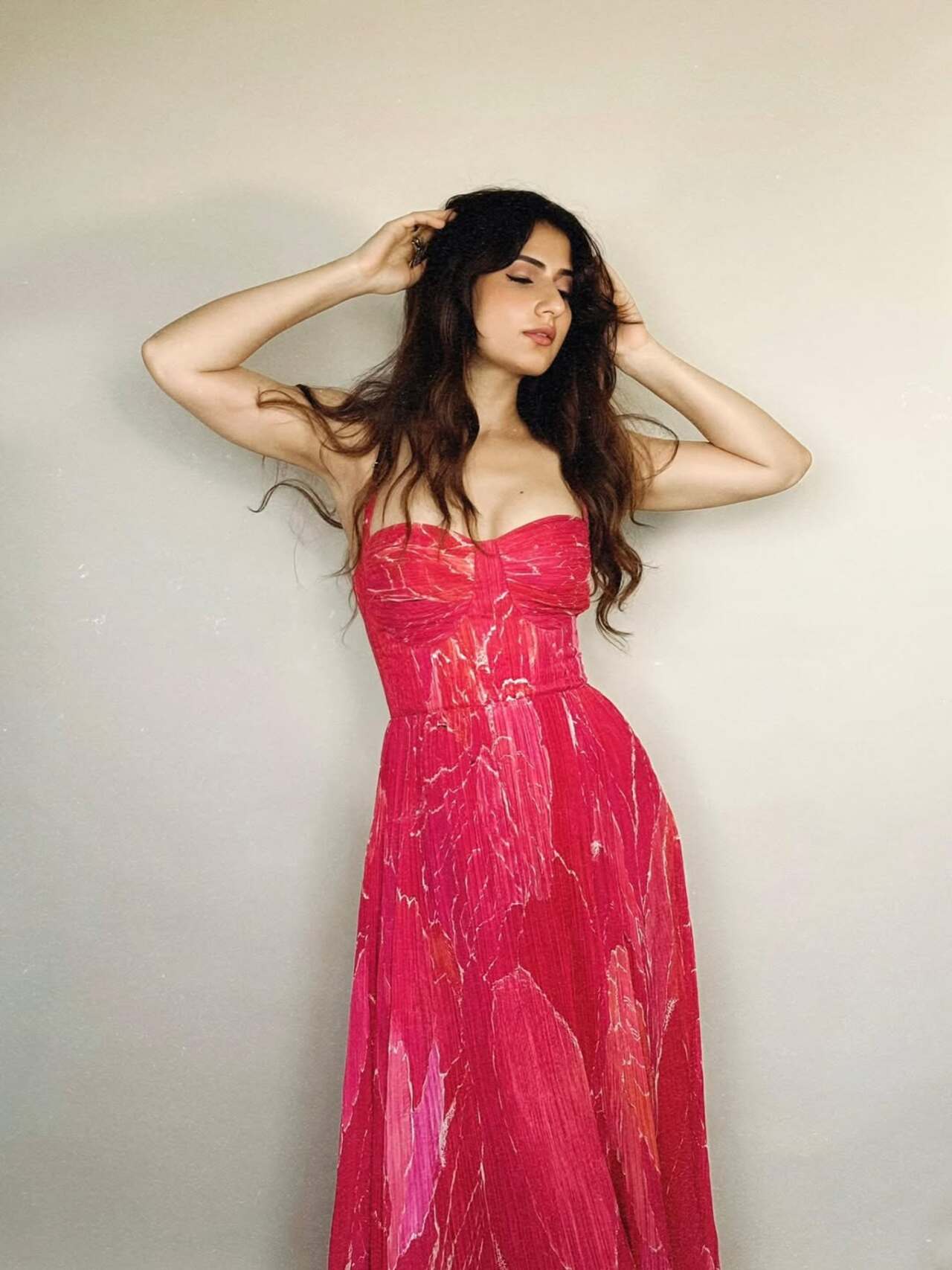 This dreamy pleated gown in painterly pinks exudes free-spirited romance. Fatima's soft waves and minimal makeup lend a breezy vibe to the look